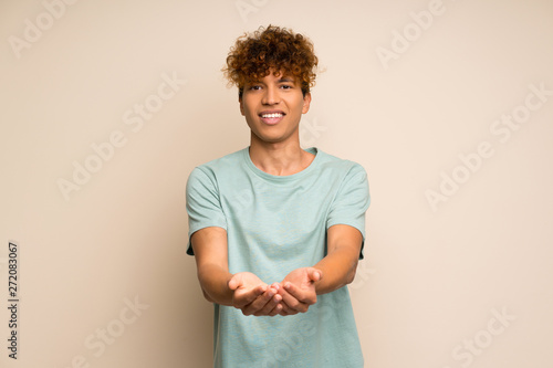 African american man with green shirt holding copyspace imaginary on the palm to insert an ad