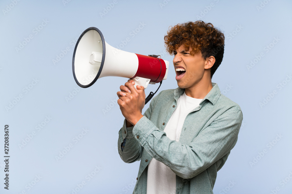 Young african american man over isolated blue wall shouting through a megaphone Young african american man over isolated blue wall shouting through a megaphone