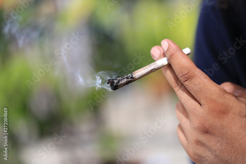 Man hand holding smokes a marijuana cannabis joint on green background, Medical marijuana should not be used in illegal ways.