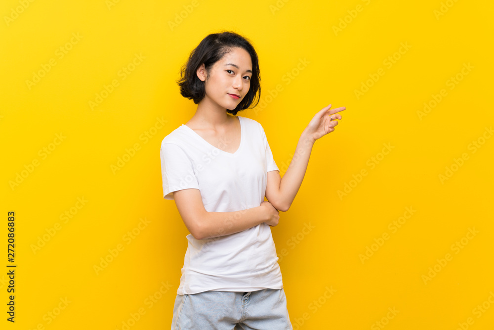 Asian young woman over isolated yellow wall pointing finger to the side Asian young woman over isolated yellow wall pointing finger to the side