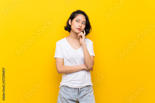 Asian young woman over isolated yellow wall thinking an idea while looking up