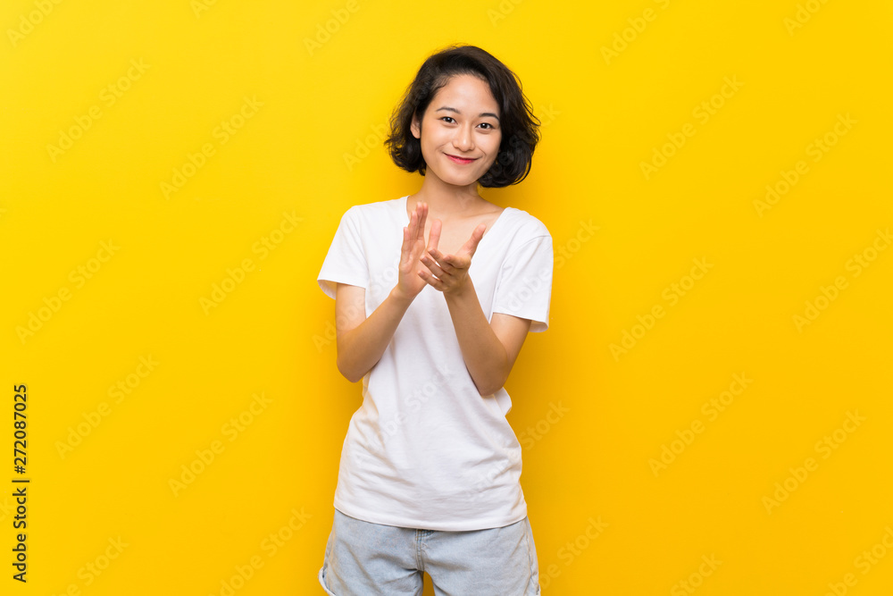 Asian young woman over isolated yellow wall applauding after presentation in a conference Asian young woman over isolated yellow wall applauding after presentation in a conference