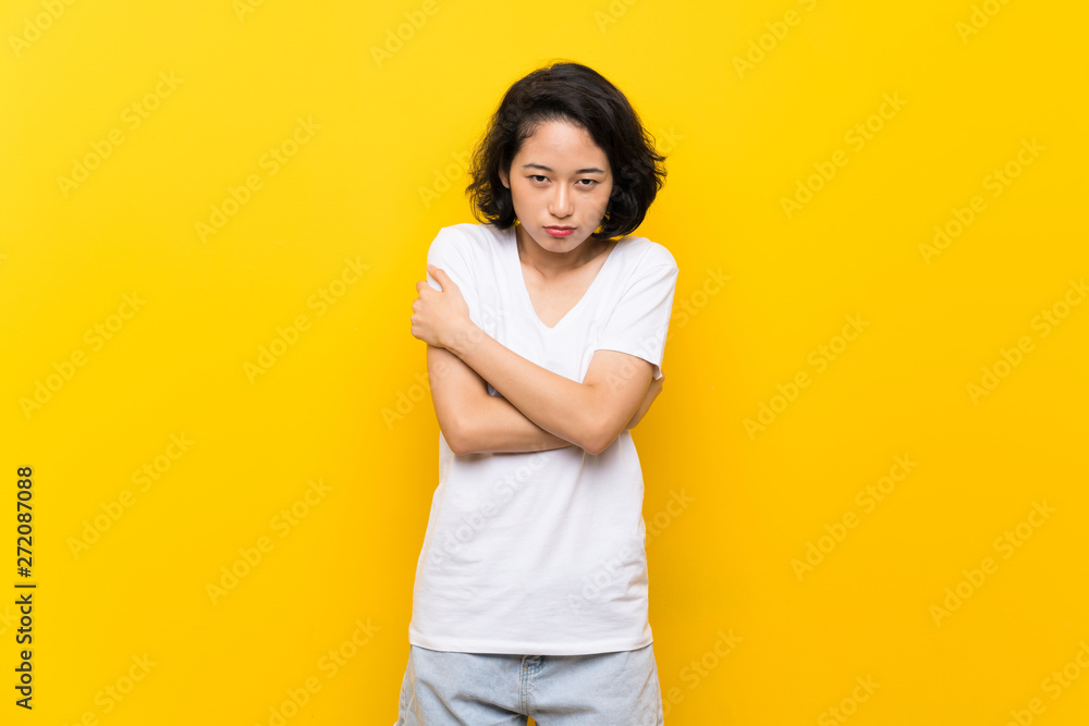 Asian young woman over isolated yellow wall freezing Asian young woman over isolated yellow wall freezing
