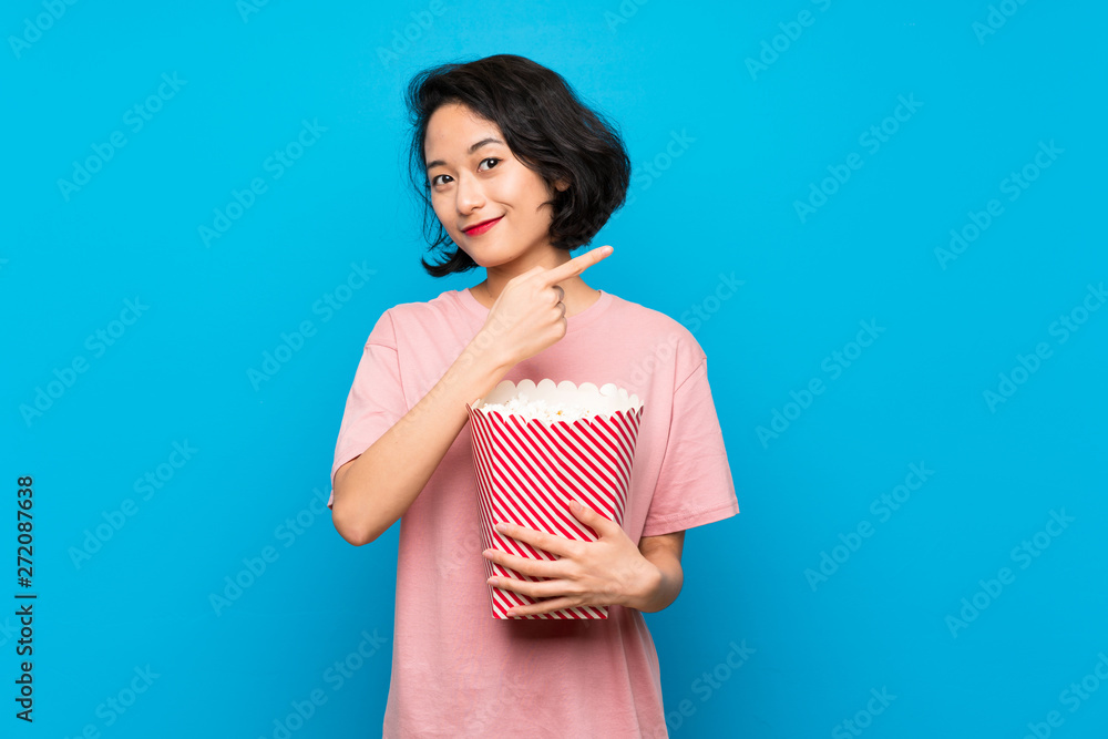 Asian young woman eating popcorns pointing to the side to present a product Asian young woman eating popcorns pointing to the side to present a product