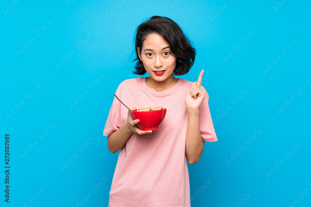 Asian young woman holding a bowl of cereals pointing up a great idea Asian young woman holding a bowl of cereals pointing up a great idea