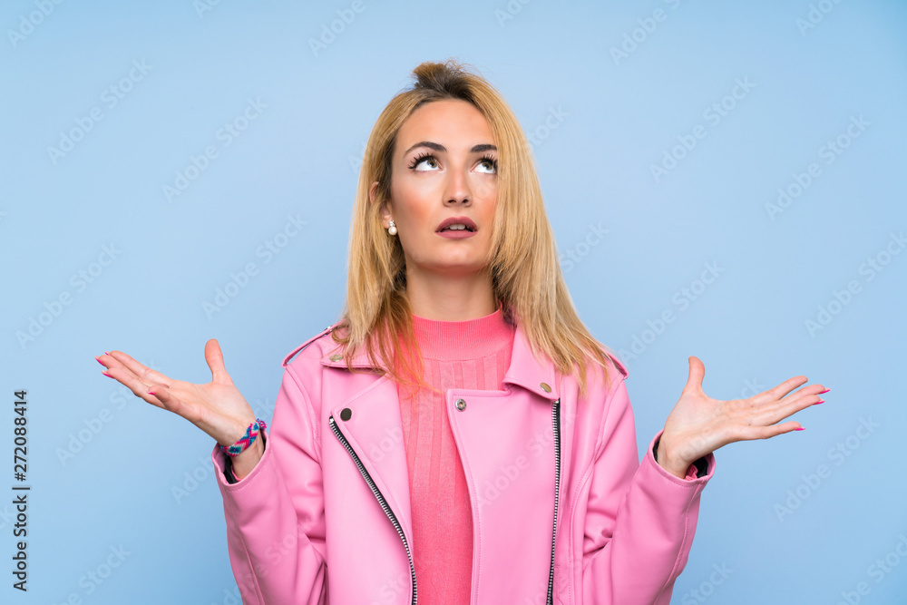 Young blonde woman with pink jacket over isolated blue background frustrated by a bad situation Young blonde woman with pink jacket over isolated blue background frustrated by a bad situation