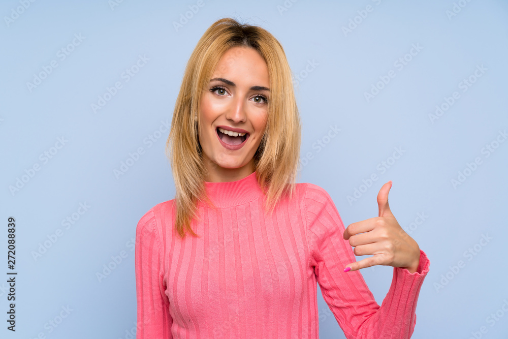 Young blonde woman with pink sweater over isolated blue background making phone gesture Young blonde woman with pink sweater over isolated blue background making phone gesture