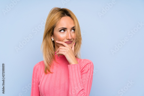 Young blonde woman with pink sweater over isolated blue background thinking an idea