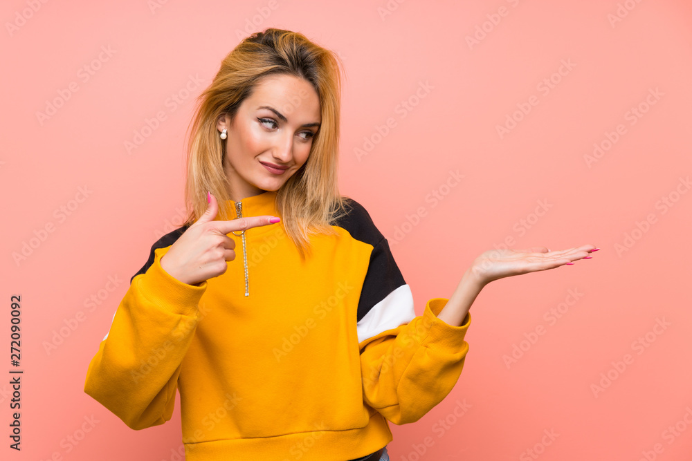 Young blonde woman over isolated pink background holding copyspace imaginary on the palm to insert an ad Young blonde woman over isolated pink background holding copyspace imaginary on the palm to insert an ad