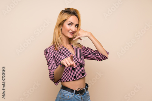 Young blonde woman with pink jacket over isolated wall making phone gesture and pointing front © luismolinero