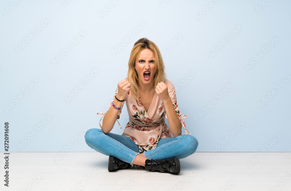 Young blonde woman sitting on the floor frustrated by a bad situation Young blonde woman sitting on the floor frustrated by a bad situation
