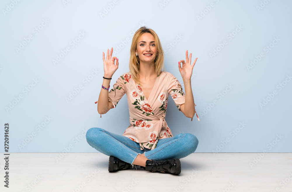 Young blonde woman sitting on the floor in zen pose Young blonde woman sitting on the floor in zen pose