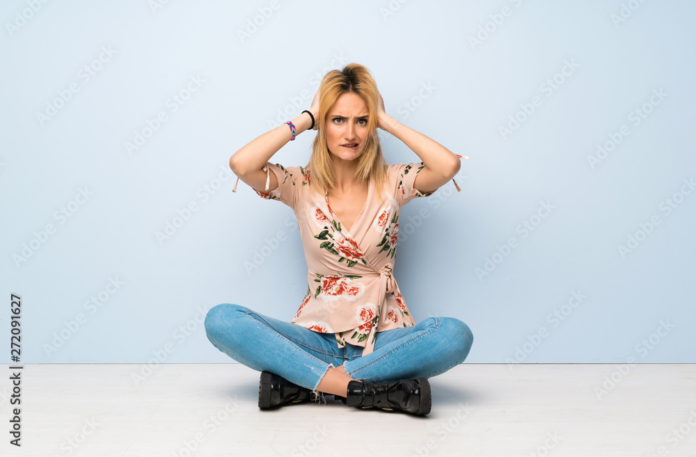 Young blonde woman sitting on the floor frustrated and takes hands on head Young blonde woman sitting on the floor frustrated and takes hands on head