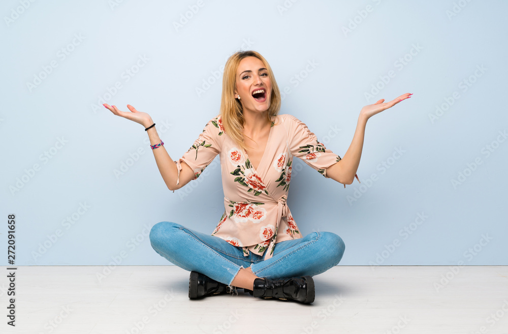 Young blonde woman sitting on the floor with shocked facial expression Young blonde woman sitting on the floor with shocked facial expression