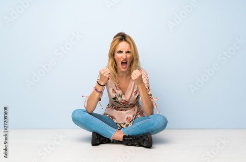 Young blonde woman sitting on the floor frustrated by a bad situation