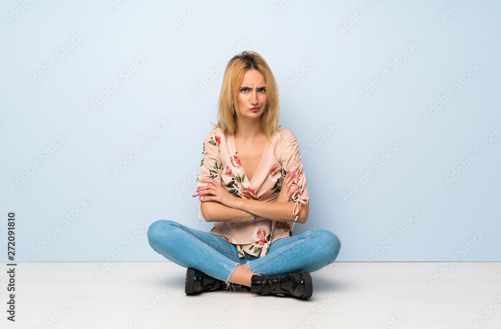 Young blonde woman sitting on the floor feeling upset Young blonde woman sitting on the floor feeling upset
