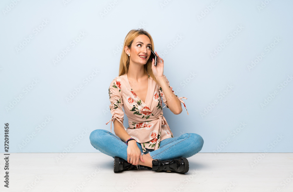 Young blonde woman sitting on the floor keeping a conversation with the mobile phone Young blonde woman sitting on the floor keeping a conversation with the mobile phone