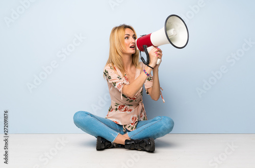 Young blonde woman sitting on the floor shouting through a megaphone