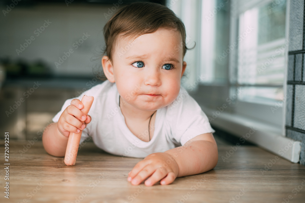 A charming little girl climbed on the table and eats a sausage with her hands A charming little girl climbed on the table and eats a sausage with her hands