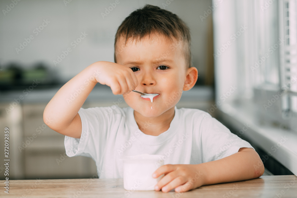 Adorable little boy eating yogurt in the kitchen in the afternoon Adorable little boy eating yogurt in the kitchen in the afternoon