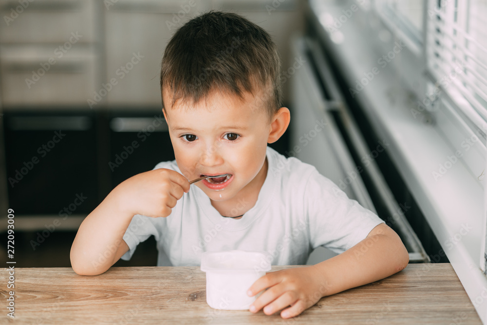 Adorable little boy eating yogurt in the kitchen in the afternoon Adorable little boy eating yogurt in the kitchen in the afternoon