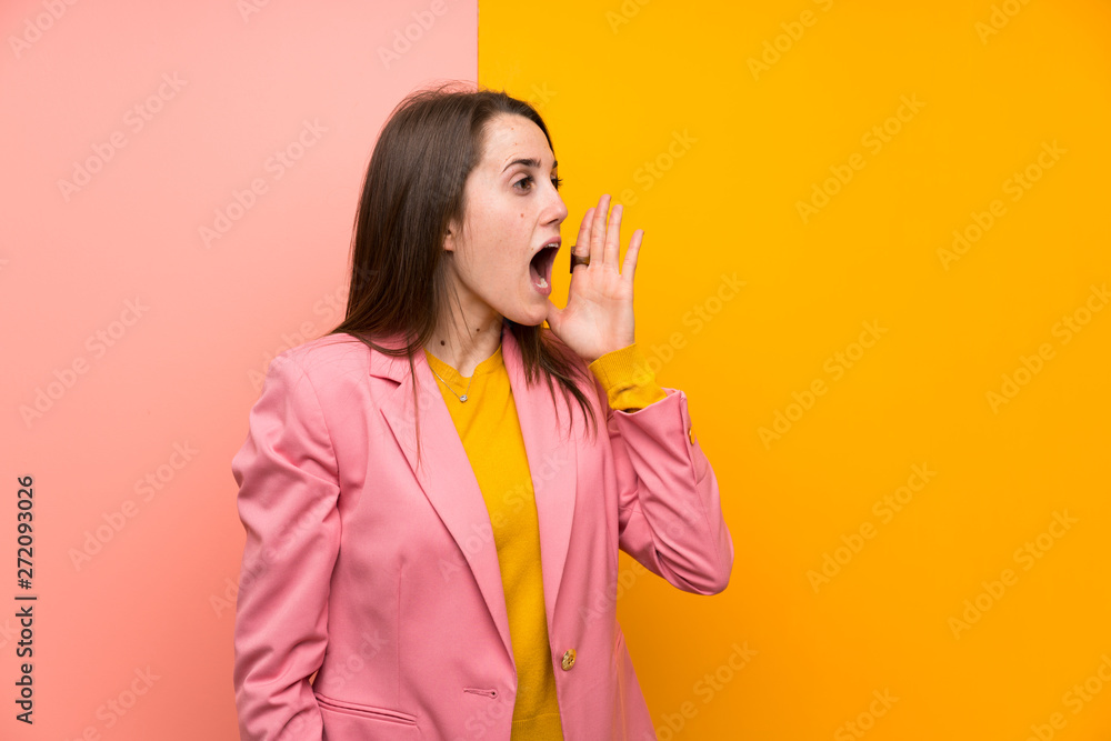 Young woman with pink suit over colorful background shouting with mouth wide open Young woman with pink suit over colorful background shouting with mouth wide open