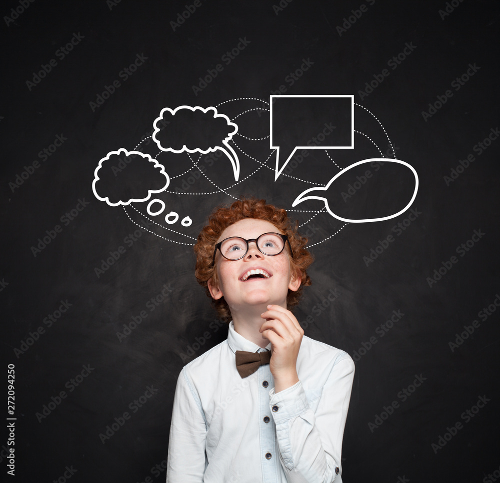 Smart kid boy with empty speech clouds bubbles at the chalkboard. Education and school concept