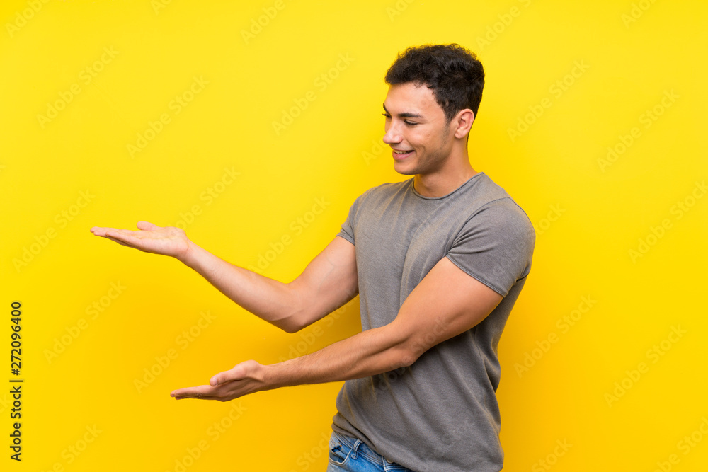 Handsome man over isolated yellow wall extending hands to the side for inviting to come Handsome man over isolated yellow wall extending hands to the side for inviting to come