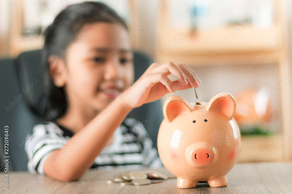 Asian little girl in putting coin in to piggy bank shallow depth of field select focus at the pig Asian little girl in putting coin in to piggy bank shallow depth of field select focus at the pig