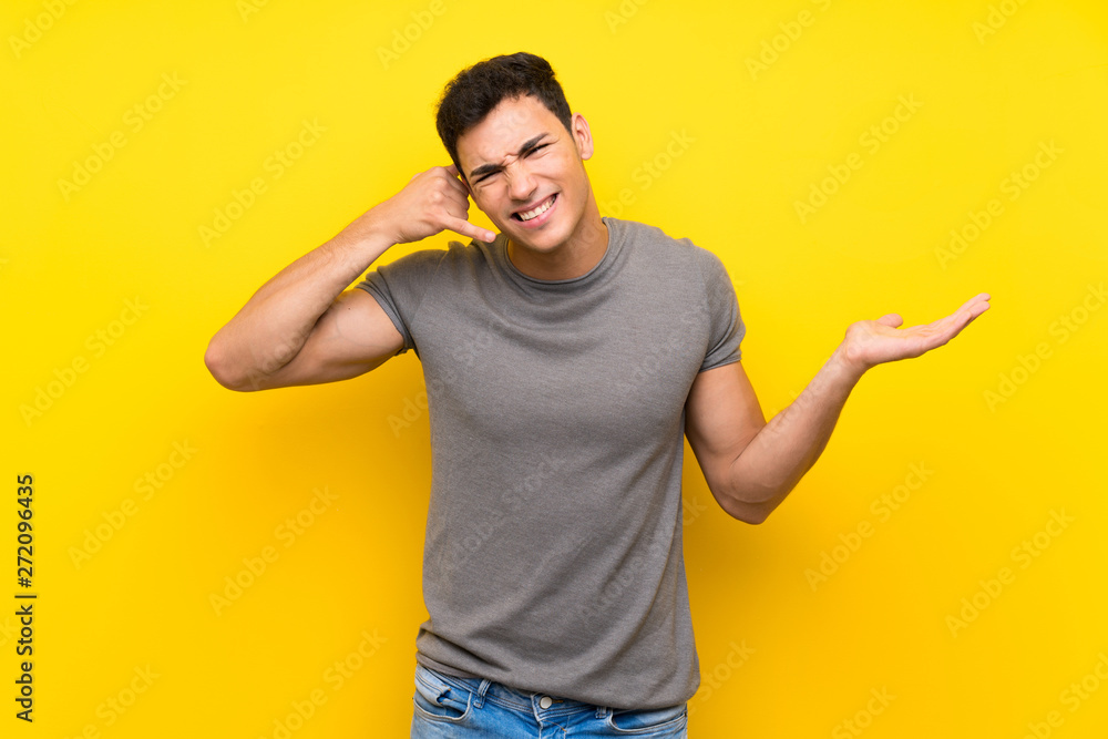 Handsome man over isolated yellow wall making phone gesture and doubting Handsome man over isolated yellow wall making phone gesture and doubting