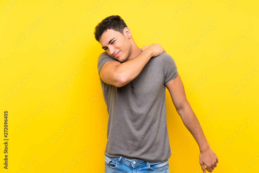 Handsome man over isolated yellow wall suffering from pain in shoulder for having made an effort Handsome man over isolated yellow wall suffering from pain in shoulder for having made an effort