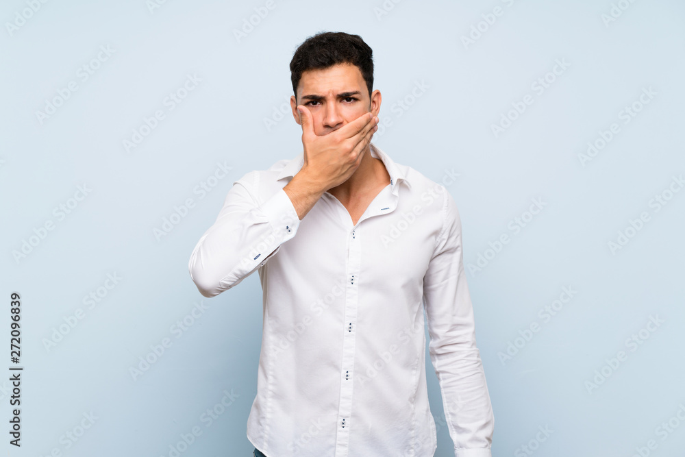 Handsome man over blue wall covering mouth with hands Handsome man over blue wall covering mouth with hands