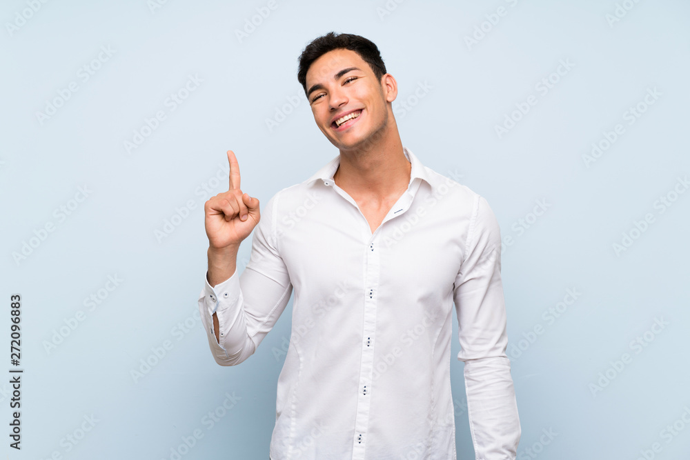 Handsome man over blue wall showing and lifting a finger in sign of the best