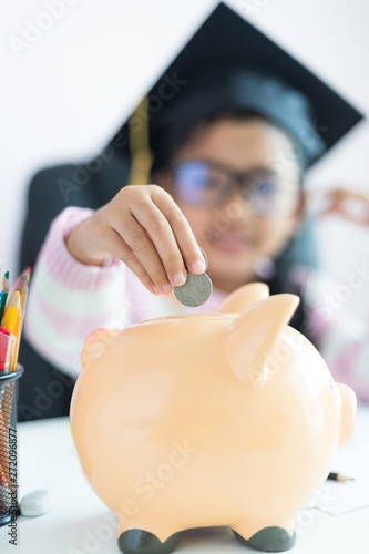 Little Asian girl putting the coin into piggy bank and smile with happiness for money saving to wealthness in the future of education concept select focus shallow depth of field photo