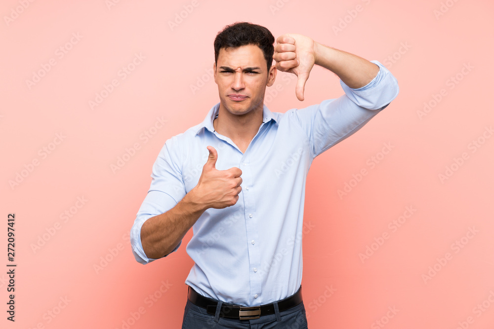 Handsome man over pink background making good-bad sign. Undecided between yes or not Handsome man over pink background making good-bad sign. Undecided between yes or not
