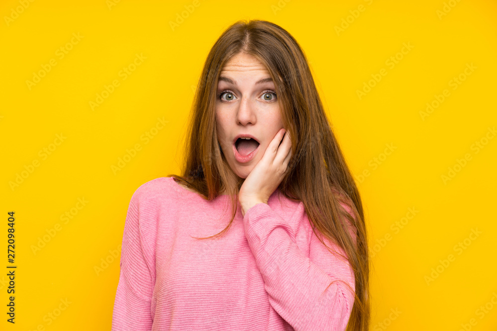 Young woman with long hair over isolated yellow wall surprised and shocked while looking right Young woman with long hair over isolated yellow wall surprised and shocked while looking right
