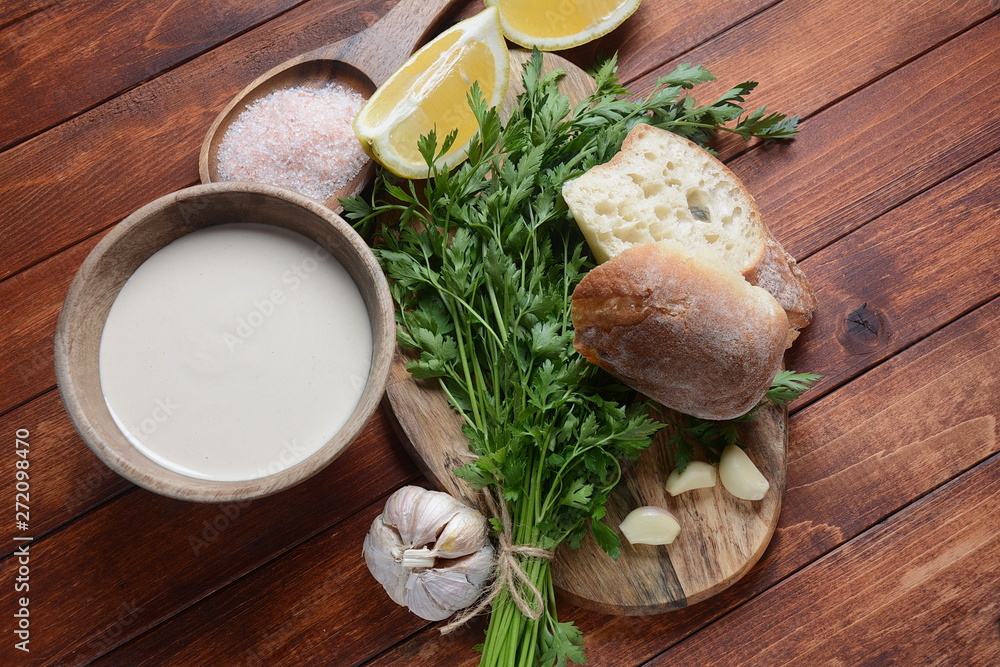 Tahini sauce made from sesame seeds in bowl with parsley on wooden background Tahini sauce made from sesame seeds in bowl with parsley on wooden background