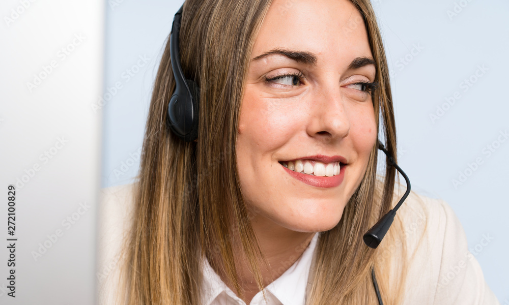 Young blonde telemarketer woman over isolated blue wall and smiling Young blonde telemarketer woman over isolated blue wall and smiling