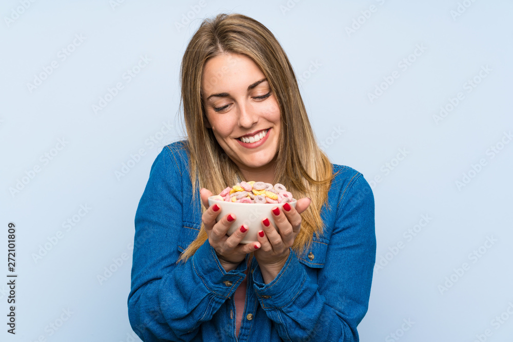 Happy young woman with bowl of cereals over isolated blue wall Happy young woman with bowl of cereals over isolated blue wall