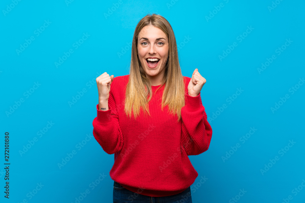 Fototapeta premium Woman with red sweater over blue wall celebrating a victory in winner position