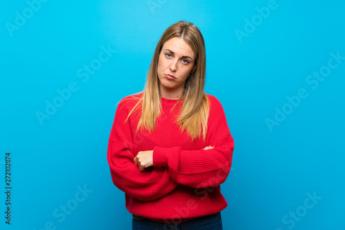 Woman with red sweater over blue wall with sad and depressed expression