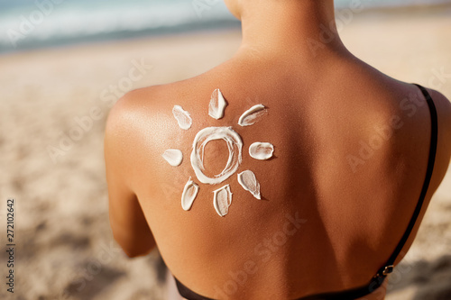 Woman Applying Sun Cream on Tanned  Shoulder In Form Of The Sun. Sun Protection.Sun Cream. Skin and Body Care. Girl Using Sunscreen to Skin. Female Holding Suntan Lotion and Moisturizing Sunblock.