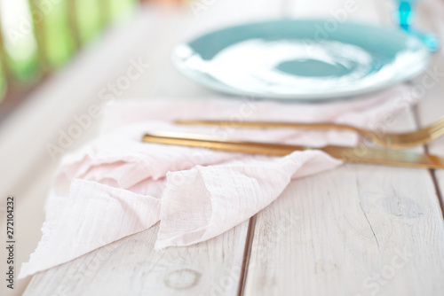 Table for guests, decorated with candles, served with cutlery and crockery and covered with a tablecloth blue plate and golden fork and knife on pink gauze napkin.