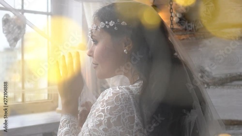 Beautiful Bride In A Dress Stands By The Window Dreaming, Smiling Charmingly