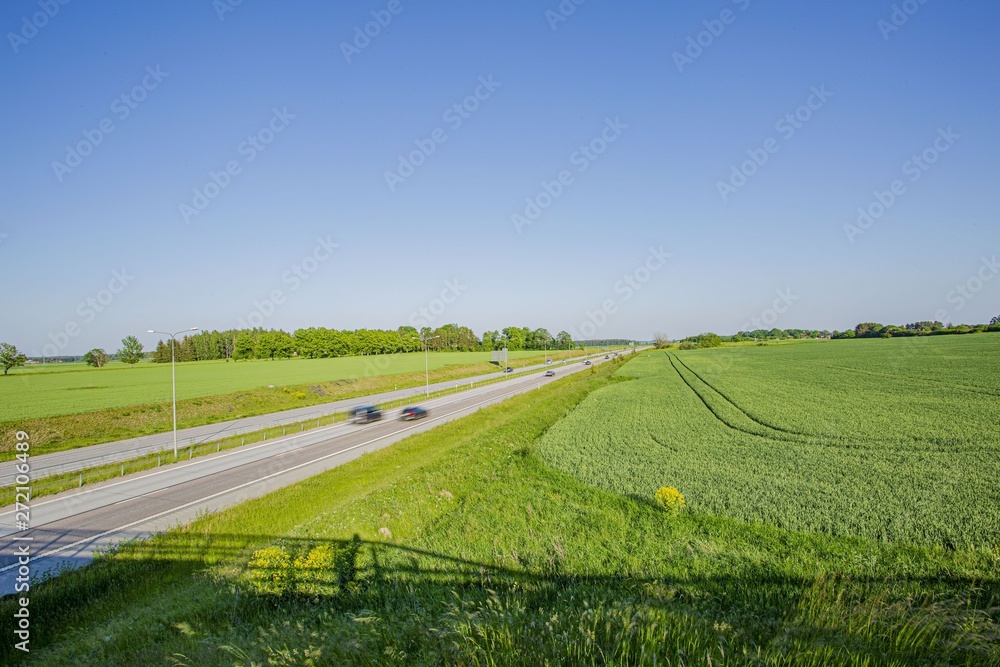 Fototapeta premium Colorful view from above on highway road with several cars. Side green fields and blue sky on bright summer day. Beautiful nature background.