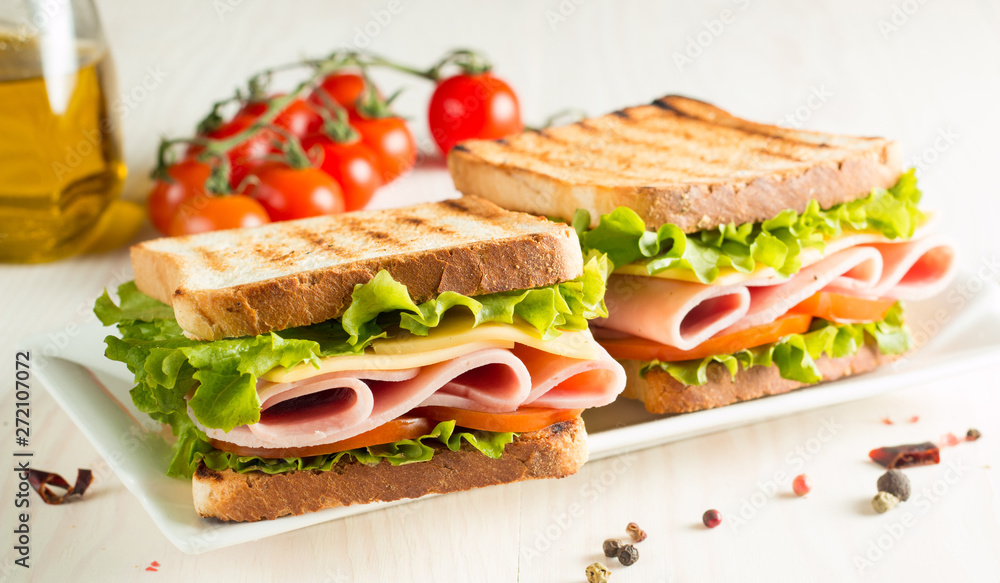 Close-up photo of a club sandwich. Sandwich with meat, prosciutto, salami, salad, vegetables, lettuce, tomato, onion and mustard on a fresh sliced rye bread on wooden background. Olives background. Close-up photo of a club sandwich. Sandwich with meat, prosciutto, salami, salad, vegetables, lettuce, tomato, onion and mustard on a fresh sliced rye bread on wooden background. Olives background.