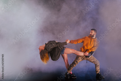 Couple dancing modern dance and showing off their leg stretch moves.Black background while the couple is dressed in urban colorful clothes..