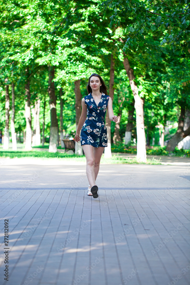 Fototapeta premium Young beautiful woman in a blue short dress walking on the road