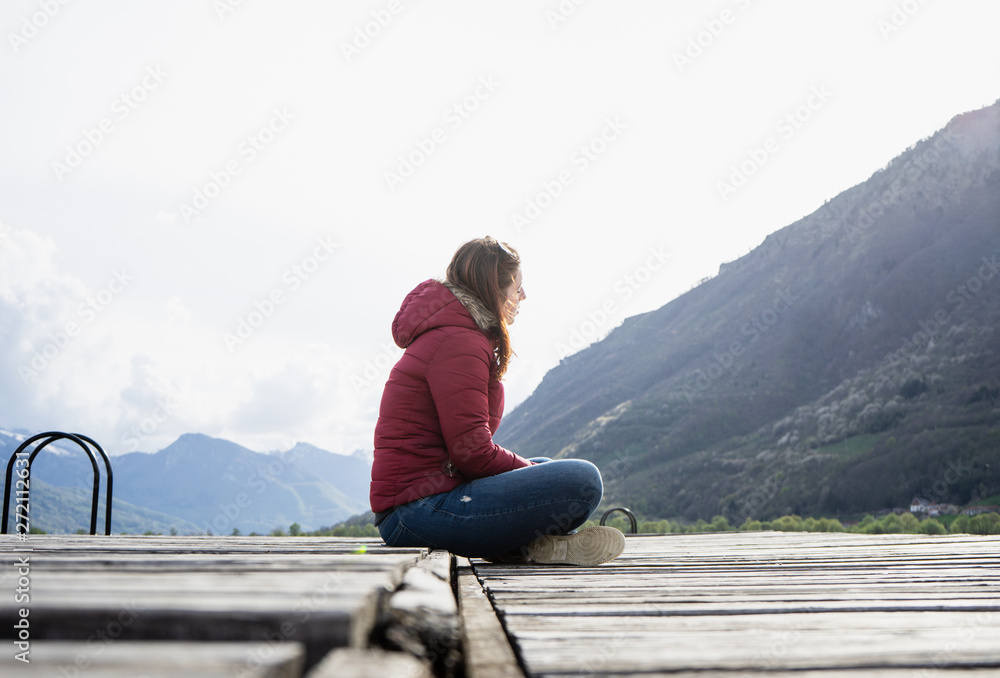 Alone women relax on wooden dock at peaceful lake. Girl meditation with red jacket in a wood pier