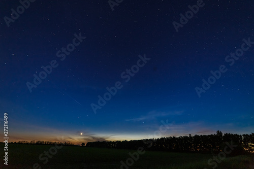 Starry sky after sunset over the field and trees. Planet Venus is above the horizon.